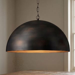 May include: A large, dome-shaped pendant light fixture with a dark, oil-rubbed bronze exterior finish and a warm, metallic gold-toned interior. The fixture is suspended from the ceiling by a matching dark metal chain and a circular mounting loop.