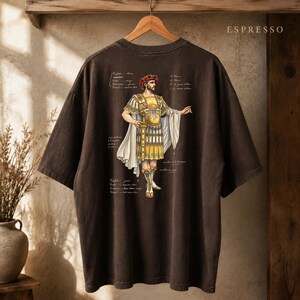 May include: A dark brown short-sleeve t-shirt featuring a graphic of a Roman figure in gold armor and a white toga, wearing a red laurel wreath. The design includes handwritten-style French text annotations around the figure and the word ESPRESSO.