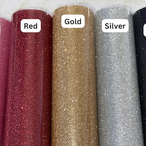 May include: Five rolls of glitter adhesive vinyl arranged side by side in pink, red, gold, silver, and black. Each roll features a white rectangular label with the corresponding color name printed in black text: Pink, Red, Gold, Silver, and Black.