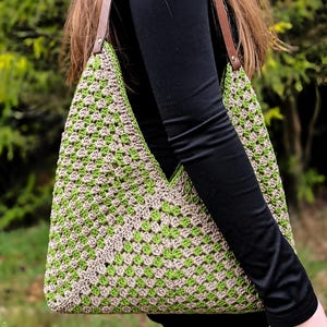 Könnte beinhalten: Handgefertigte Häkeltasche im Granny-Square-Muster. Die Tasche hat eine Kombination aus grüner und beiger Wolle mit braunen Lederriemen. Die Tasche wird über der Schulter getragen.