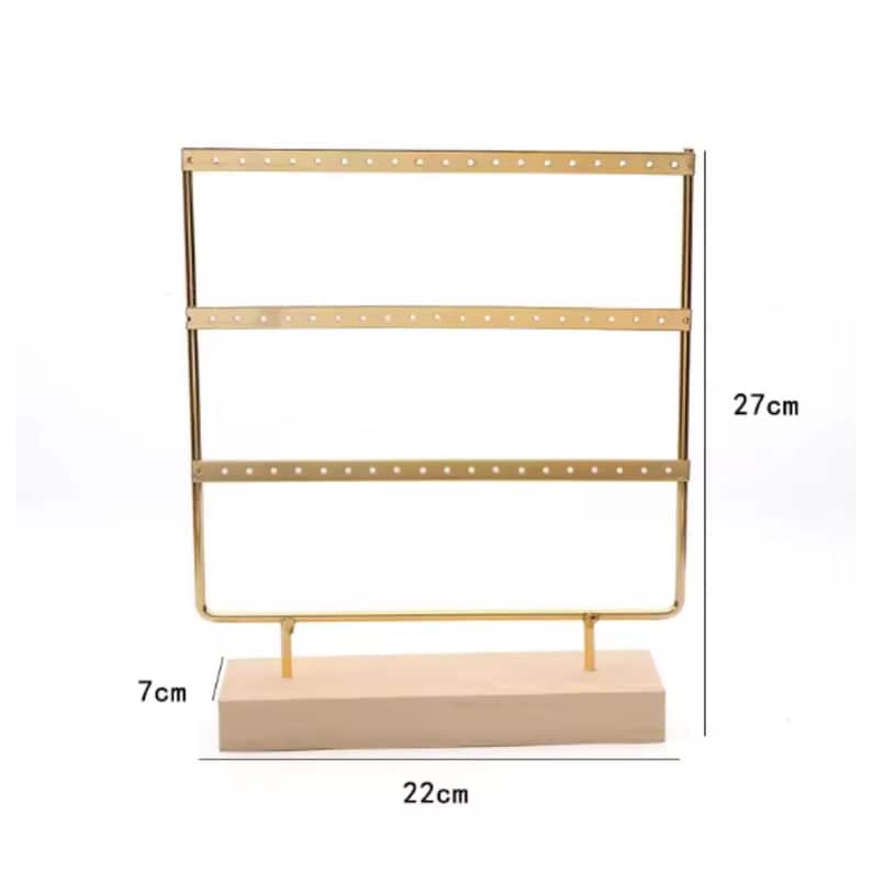 May include: A gold-colored metal earring display stand with three horizontal bars, each with multiple holes for earrings. The stand is 27 cm tall, 22 cm wide, and has a 7 cm wooden base.