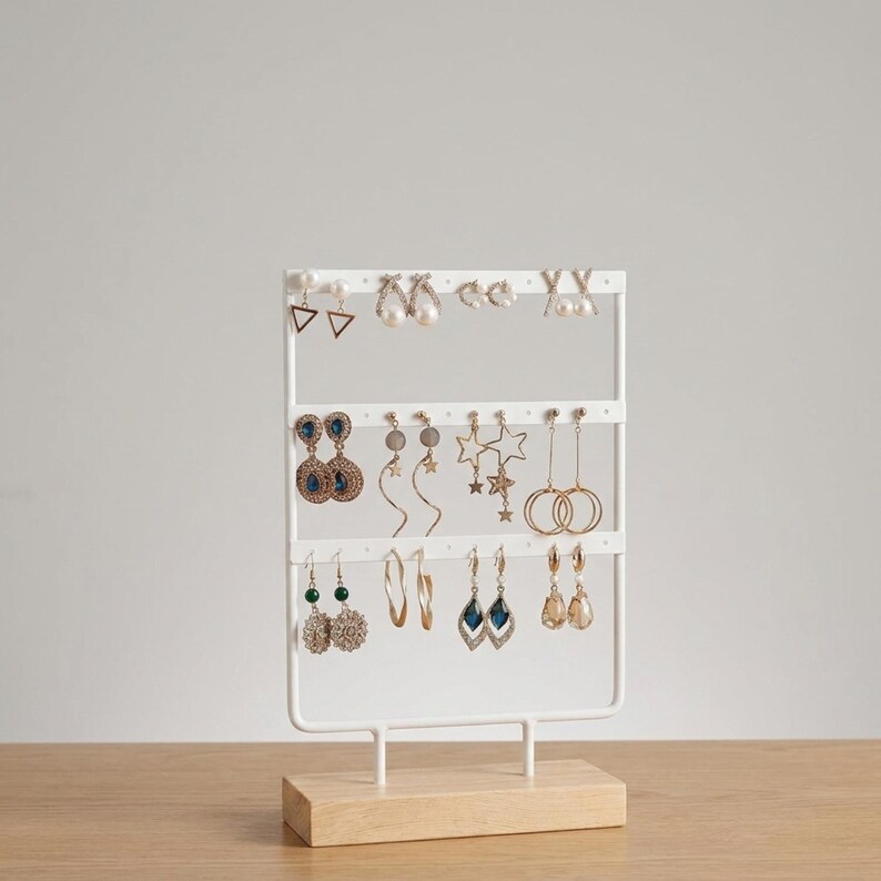 May include: A white metal earring display stand with multiple pairs of earrings. The stand has a rectangular wooden base and a grid-like structure to hold the earrings. Various earring styles include studs, hoops, and dangling designs in gold, silver, and blue.