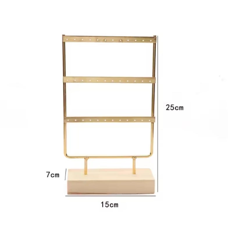 May include: A gold-colored metal earring display stand with three horizontal bars, each with multiple holes. The stand is 9.8 inches tall, 5.9 inches wide, and sits on a 2.8-inch wooden base.