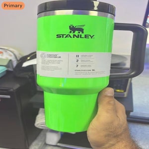 Peut inclure: Un gobelet isotherme vert néon vif avec une poignée et un couvercle noirs. L'avant présente le logo Stanley noir et une étiquette blanche détaillant le couvercle FlowState à 3 positions, indiquant 11 heures froid, 2 jours glacé, 7 heures chaud.