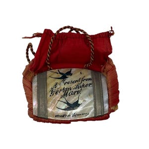 May include: A small red fabric pouch featuring a central rectangular mother-of-pearl inlay. The inlay displays two black swallow illustrations and the text "A Present from Weston-super-Mare" and "made in Germany" in black script lettering.