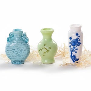 May include: Three small decorative vases. The first is light blue with a cracked pattern and ornate handles. The second is light green with a floral design. The third is white with a blue floral pattern. All are ceramic.
