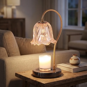 May include: A decorative table lamp with a flower-shaped glass shade and a gold-colored metal frame. The lamp sits on a marble base, with a candle in a glass holder. A small vase and a book are also on the table.