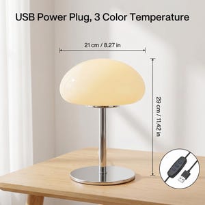May include: A mushroom-shaped desk lamp with a USB power plug and 3 color temperature settings. The lamp is 11.42 inches tall and 8.27 inches wide. The lamp has a chrome base and stem, and a cream-colored shade. The text "USB Power Plug, 3 Color Temperature" is visible.