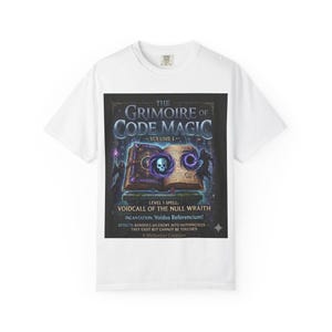 Op de afbeelding: Wit T-shirt met een afbeelding van "The Grimoire of Code Magic, Volume I." Het ontwerp toont een open boek met een schedel, wervelende paarse energie en de tekst "Voidcall of the Null Wraith."