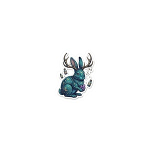 May include: A sticker featuring a teal rabbit with antlers, adorned with crescent moons and stars. The rabbit holds a purple crystal and is surrounded by small potion bottles and dangling charms. The design has a whimsical, magical theme.