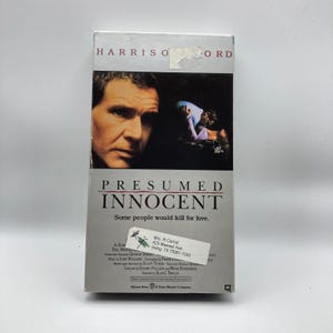 May include: A VHS tape for the movie "Presumed Innocent" featuring Harrison Ford. The cover has a close-up of Ford's face and a scene from the film. The title and tagline "Some people would kill for love" are also visible.