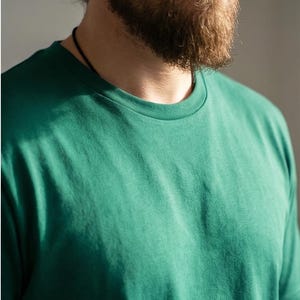 Könnte beinhalten: Nahaufnahme eines grünen T-Shirts mit Rundhalsausschnitt. Das Shirt ist einfarbig und scheint aus einem weichen Material zu sein. Das Bild zeigt den oberen Brust- und Schulterbereich des Shirts.