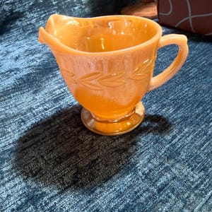 May include: A white ceramic mug with a black handle and the text "But First, Coffee" in a black, bold font. The mug is sitting on a wooden surface. The mug is 4 inches tall.