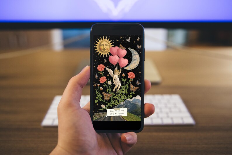 Hand holding a phone showing a mixed media collage wallpaper with celestial and botanical art in a cozy room setting
