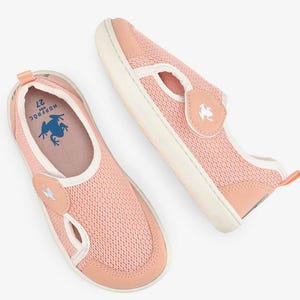 May include: Pair of pink mesh slip-on shoes for kids. The shoes have a white sole and trim, with a peach-colored accent on the toe and heel. A small patch with a frog logo is on the side. The insole has a blue frog graphic and the number 27.