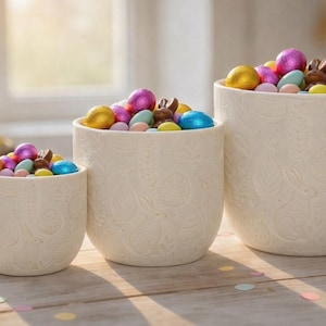 Peut inclure: Ensemble de trois tasses en céramique avec une finition mate et mouchetée. Les tasses sont de couleurs crème, gris clair et gris foncé. Chaque tasse a un design simple et minimaliste.