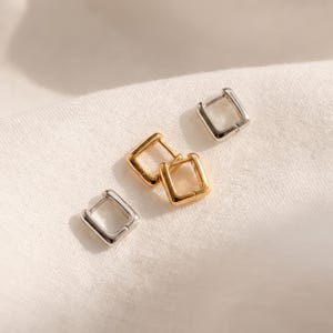 May include: A set of four small square hoop earrings, featuring two polished silver-tone hoops and two polished gold-tone hoops. Each earring has a hinged closure mechanism, creating a clean, geometric shape with rounded corners and a smooth finish.
