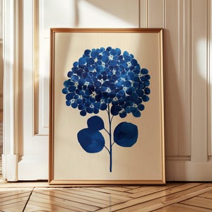 Könnte beinhalten: Gerahmter Kunstdruck mit einer blauen Hortensienblüte. Das Kunstwerk hat einen goldenen Rahmen und einen cremefarbenen Hintergrund. Die Blütenblätter der Blume sind tiefblau. Geeignet für die Inneneinrichtung.