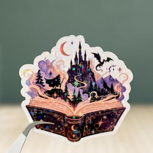May include: A die-cut sticker featuring an open book with a magical scene emerging from its pages, including a dark castle, a flying dragon, a silhouetted figure, pine trees, and a crescent moon, all accented with holographic star details.