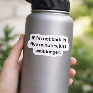 May include: A gray stainless steel water bottle with a black lid and handle. A white sticker on the bottle reads, "If I'm not back in five minutes, just wait longer."