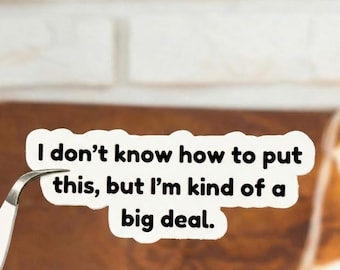May include: A white sticker with the text "I don't know how to put this, but I'm kind of a big deal." The sticker is being held by a pair of silver tweezers, against a brown background.
