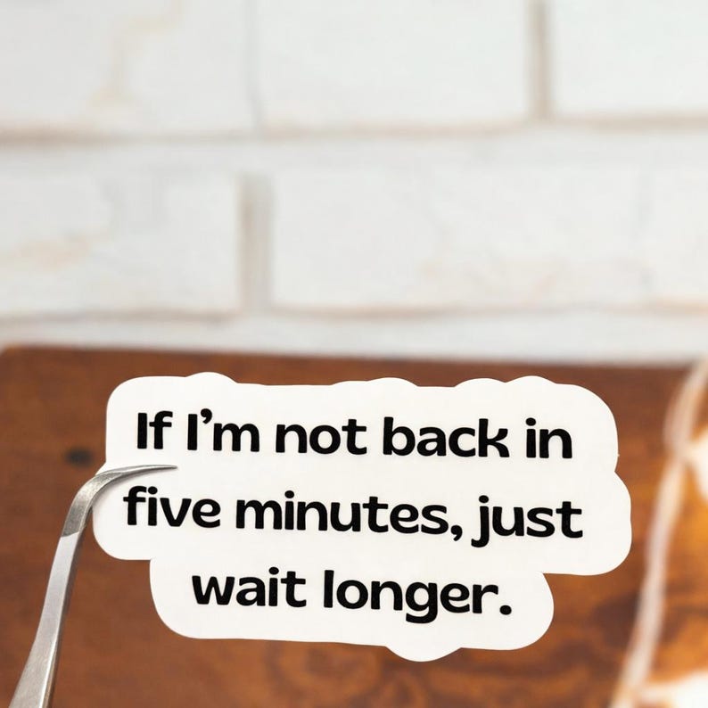 May include: A white sticker with the text "If I'm not back in five minutes, just wait longer." The sticker is held by a pair of silver tweezers against a brown surface and a white brick wall background.