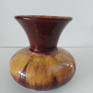 May include: A ceramic vase with a rounded base and a flared top. The vase has a colour gradient, going from dark brown at the top to lighter brown and tan on the base. The glossy finish enhances the colours.