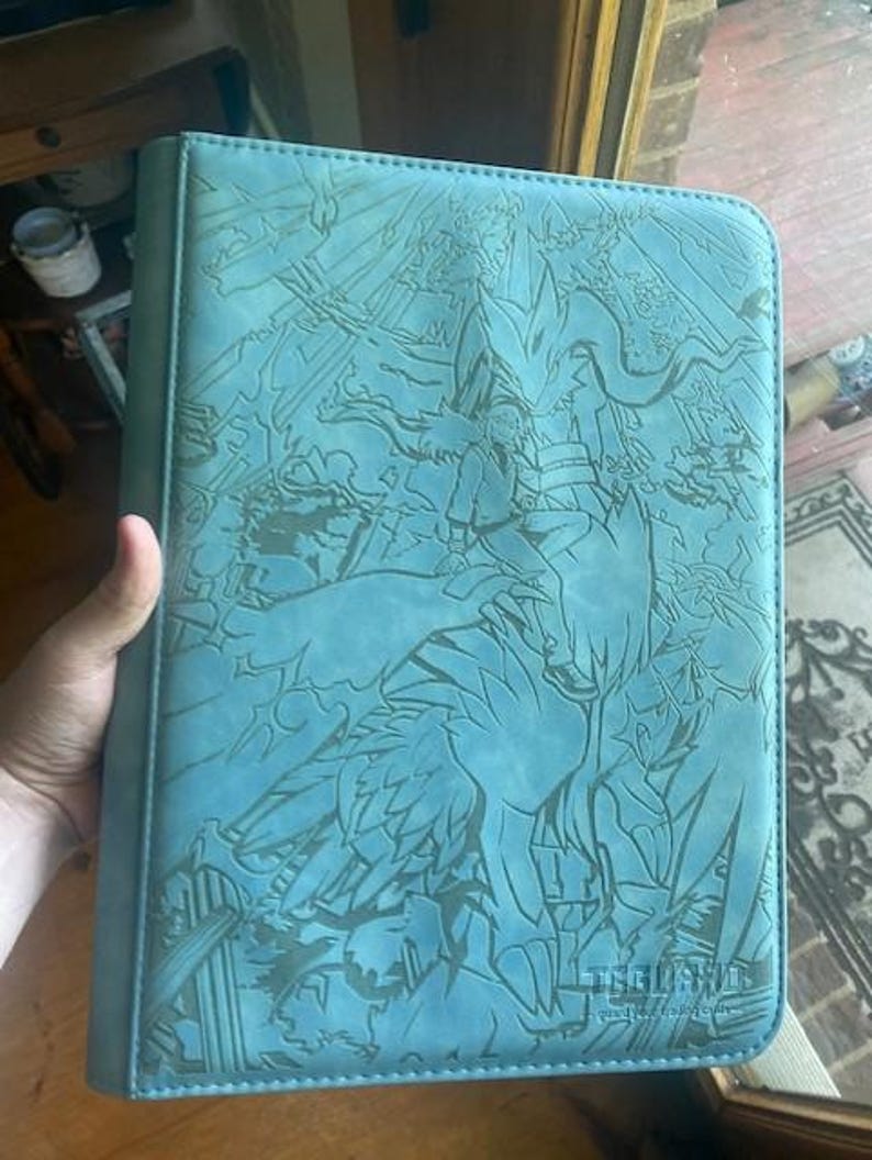 May include: A light blue rectangular trading card binder featuring an intricate laser-engraved illustration of a character riding a large creature. The bottom right corner displays the text "TEGLAND" with the subtitle "guard your trading cards".