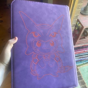 May include: A rectangular purple binder featuring a laser-engraved outline of a character wearing a hooded costume. The design depicts a small creature with pointed ears and a round body, centred on the front cover with visible stitching along the edges.