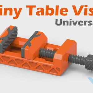 Puede incluir: Un tornillo de banco de mesa pequeño naranja con detalles en gris y la palabra "Universal!" en gris. El tornillo de banco tiene un mecanismo de tornillo para ajustar el agarre. El texto "Tiny Table Vise" es naranja.