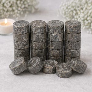 May include: A collection of grey stone game pieces, cylindrical in shape, stacked in columns. The pieces have a marbled appearance and are arranged on a light surface. Some pieces are scattered around the columns.
