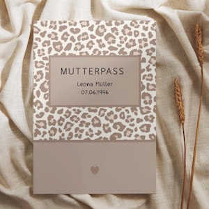 Könnte beinhalten: Ein rechteckiger Mutterpass-Umschlag mit einem beigefarbenen und braunen Leopardenmuster auf der oberen Hälfte und einer einfarbigen hellbraunen Fläche auf der unteren Hälfte. Der Text lautet MUTTERPASS, Leona Müller, 07.06.1996, mit einem Herz.