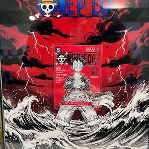 May include: Framed One Piece artwork featuring a red background with black storm clouds and lightning. The artwork includes a card with a Luffy illustration and Japanese text. The One Piece logo is at the top.