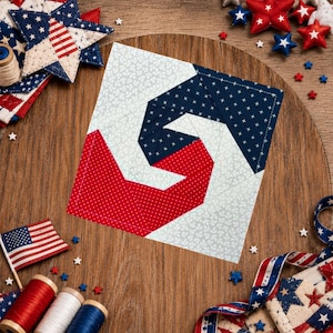 May include: A patriotic-themed quilted coaster with a red, white, and blue spiral design. The coaster is surrounded by star-shaped decorations, spools of thread, and a small American flag, all on a wooden surface.
