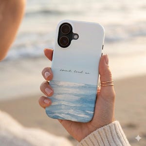 May include: A white phone case with a watercolor design of a blue ocean and sky. The case has the words "Spirit lead me" in a delicate script. The phone case is held in a hand.