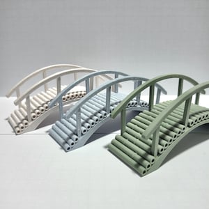 May include: Three miniature arched bridges arranged in a row, each featuring a curved railing and a deck constructed from cylindrical segments. The bridges are colored in off-white, light blue, and sage green, showcasing a textured finish.