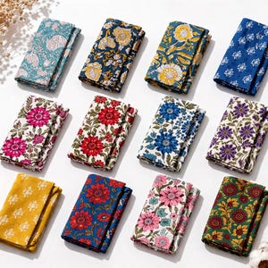 Puede incluir: Un surtido de artículos de tela floral plegados en varios colores, incluyendo turquesa, azul marino, amarillo, azul, rosa, rojo y verde. Cada artículo presenta un patrón floral diferente, con fondos blancos. Los artículos están dispuestos sobre una superficie blanca.