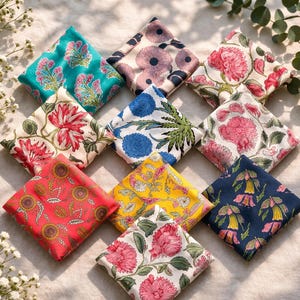Könnte beinhalten: Eine Auswahl an farbenfrohen, quadratischen Stoffservietten mit floralen Mustern. Die Servietten zeigen verschiedene Designs, darunter Sonnenblumen, Pfingstrosen und andere botanische Motive in Rot-, Blau-, Gelb- und Rosatönen.