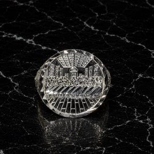 May include: A circular silver-toned ring featuring a detailed embossed relief of The Last Supper scene. The face of the ring has a polished, reflective finish with a diamond-cut border that catches the light, creating a bright, metallic appearance.