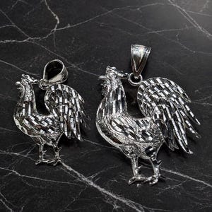 Puede incluir: Dos colgantes de gallo en tono plateado con un acabado texturizado de corte de diamante en el cuerpo y las plumas de la cola. Cada colgante incluye una anilla pulida en la parte superior para una cadena, con un diseño aviar muy detallado.