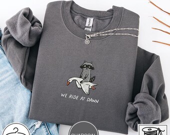 Sudadera bordada "We Ride At Dawn", sudadera divertida de mapache montando un ganso, camiseta bordada de lindo caballero animal, regalo de mapache guerrero