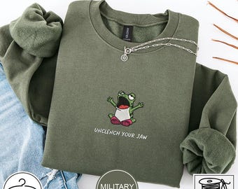 Sudadera bordada con la frase "Unclench Your Jaw" (Abre la mandíbula) y la rana, marca Gildan 18000.
