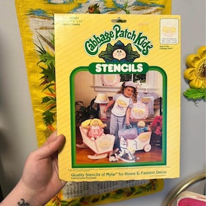 May include: A vintage Cabbage Patch Kids stencil set in a yellow and green package. The package features an image of a girl with Cabbage Patch Kids dolls and the text "STENCILS". The stencil set is for home and fashion decor.