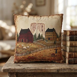 May include: A square throw pillow featuring a printed autumn landscape scene with a red house, a yellow house, a weeping willow tree, white fences, grazing sheep, pumpkins, and a scarecrow, all set against a cream-coloured background.