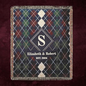 May include: A woven throw blanket featuring a dark argyle pattern in shades of navy, green, and burgundy with cream diamonds. The center displays a large cream letter S inside a diamond frame, with the text Elizabeth & Robert EST. 2026 below.