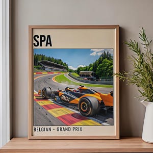 May include: A framed print depicting a Formula 1 car on a race track. The car is orange and black, with "OKX" visible. The print includes the text "SPA" and "BELGIAN - GRAND PRIX". The track is surrounded by trees.