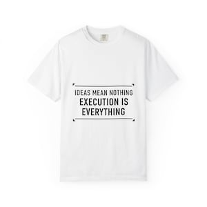 May include: White t-shirt with the text "IDEAS MEAN NOTHING EXECUTION IS EVERYTHING" in a black rectangular frame. The shirt has a crew neck and short sleeves. The shirt is made of a soft, comfortable material.