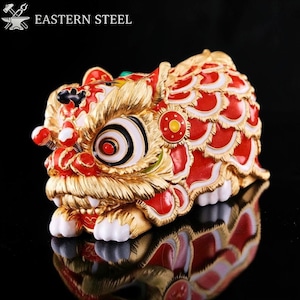 May include: A detailed, gold-colored lion dance figurine with red and white accents. The figurine has a detailed design, with a focus on the face and body. The text "EASTERN STEEL" is in the upper left corner.