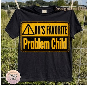 May include: Black t-shirt with a yellow and black graphic that reads "HR'S FAVORITE Problem Child". The design resembles a warning sign. The shirt is hanging on a clothesline with a natural background.