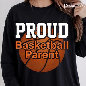 Puede incluir: Camiseta negra de manga larga con las palabras "PROUD Basketball Parent" en blanco y naranja. La palabra "PROUD" está en negrita, con un gráfico de baloncesto en el centro.